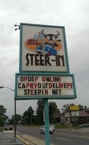 the sign of the Steer-In restaurant, featuring a horned steer in a convertible