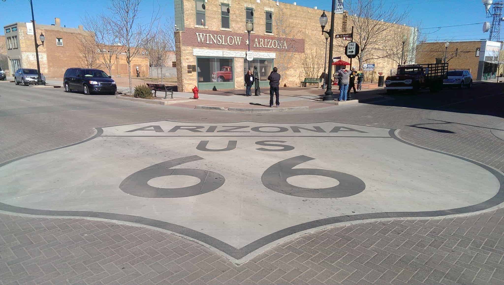 Route 66 icon painted on street in front of mural of girl in flatbed ford and bronze statue