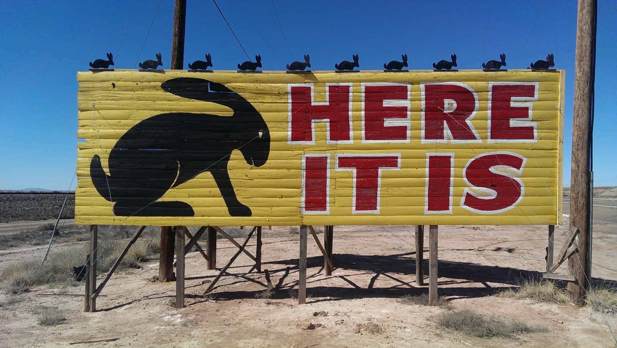 yellow sign with black rabbit silhouette and words HERE IT IS