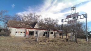decrepit building with empty sign, surrounded by scraggly weeds and utterly forlorn