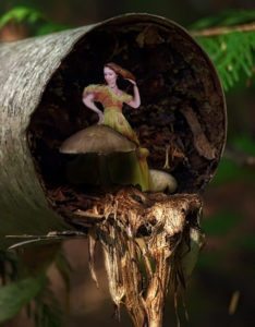 Tiny Laura in green dress with mushroom inside hollow tree trunk