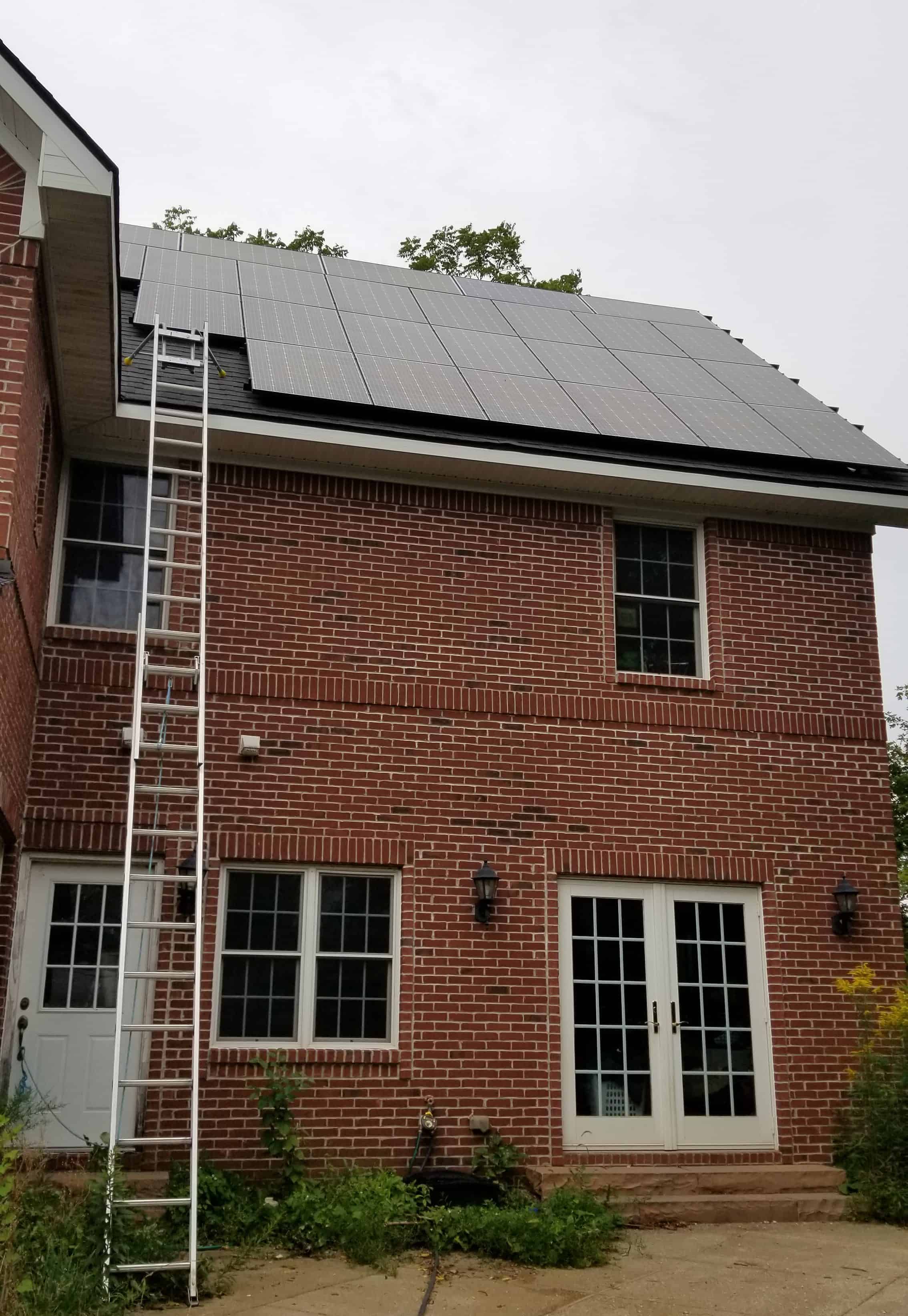 two-story brick house with ladder to roof and solar panels