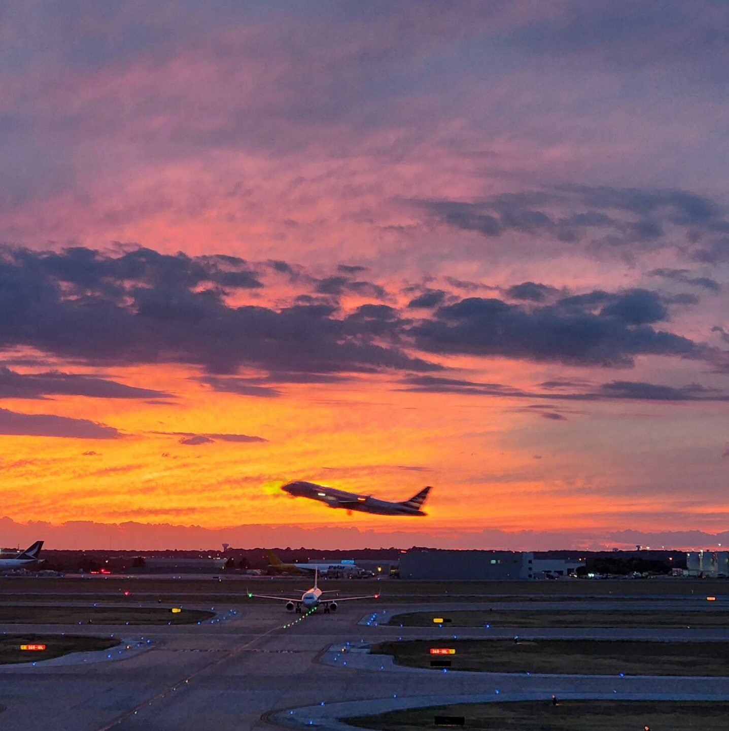 a plane taking off in silhouette before a red sunset